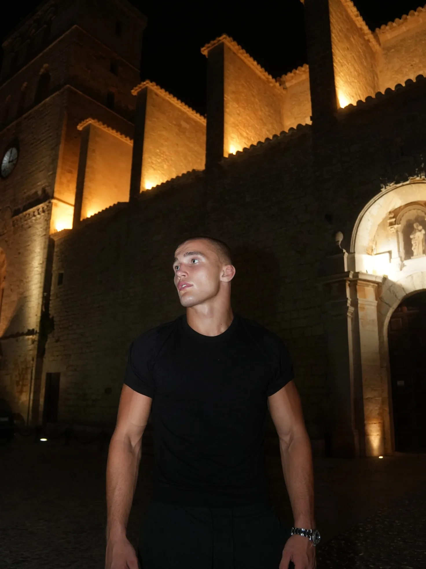 Moritz Barth im schwarzen T-Shirt steht nachts vor einer beleuchteten alten Burgmauer.